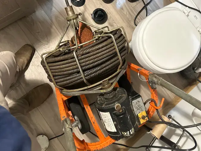 Professional sewer machine used to clear a clogged drain near a toilet