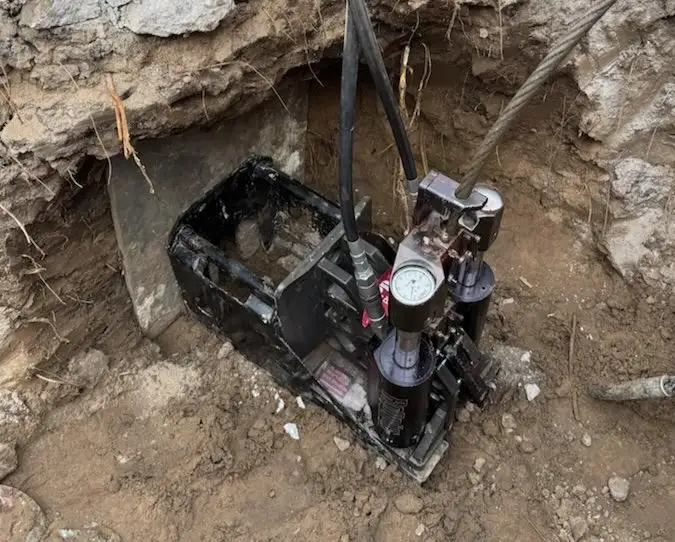 Trenchless pipe-bursting equipment positioned in a sewer access pit beneath concrete