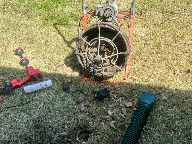 Roots and debris removed from a main sewer line beside professional cleaning equipment