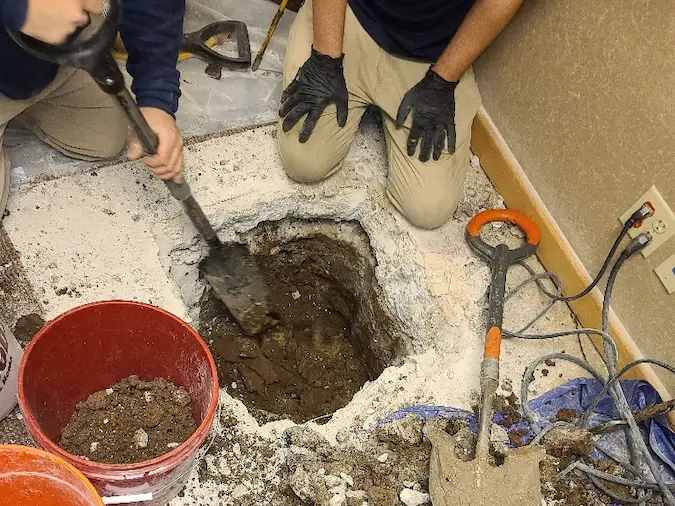 Technicians opening an interior concrete slab to access a sewer repair