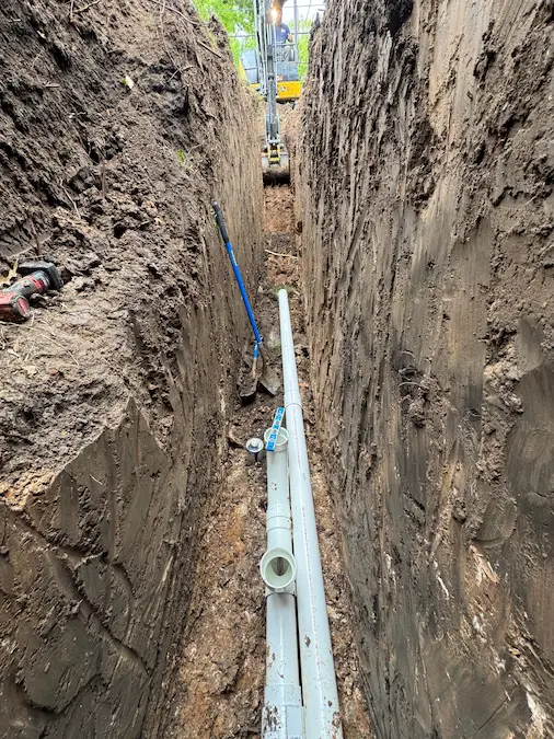 New PVC sewer line being checked for grade inside an open trench