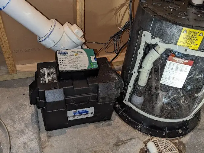 Battery backup sump pump system installed beside a sump basin